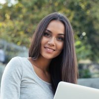 Portrait of a cheerful female student sitting on the city stairs and using laptop computer outdoors